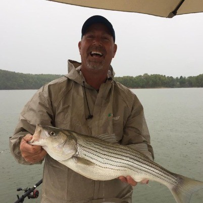Captain Billy Genay laughing on the boat while holding a freshly caught fish.
