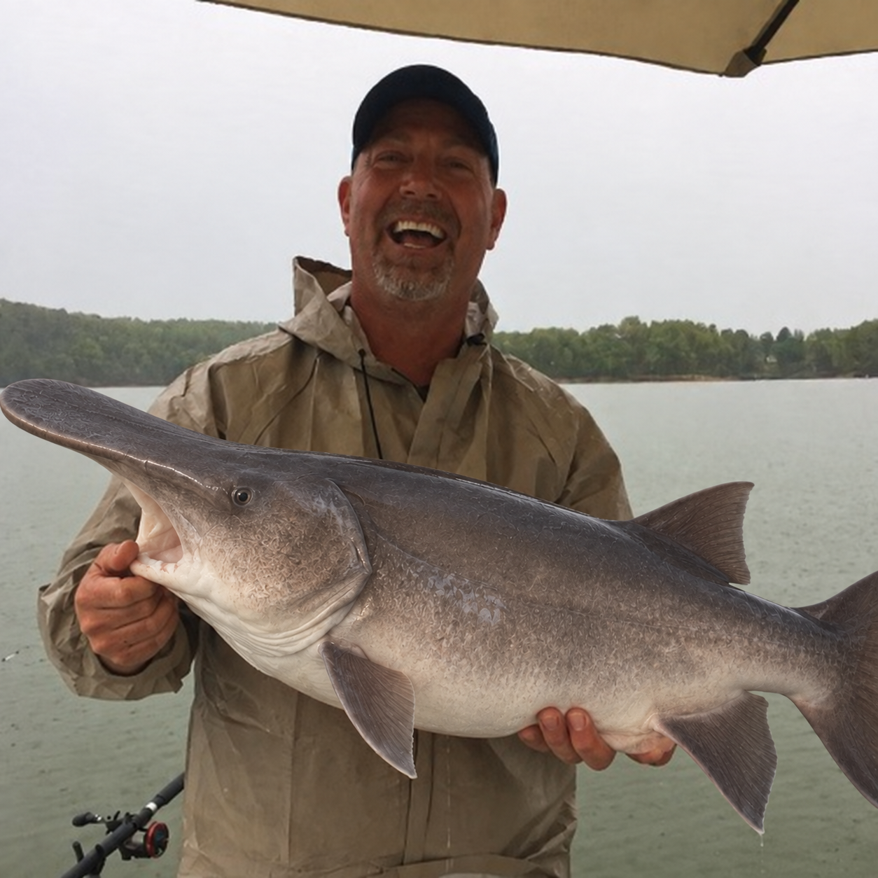 Captain Billy Genay laughing on the boat while holding a large paddlefish, open water and a wooded shoreline behind him.